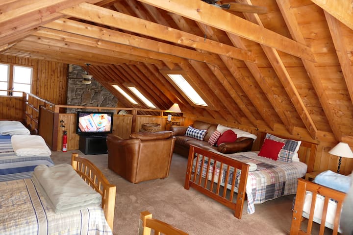 غرفة نوم علوية مع ستة أسرّة مزدوجة ومقاعد وتلفزيون بشاشة مسطحة