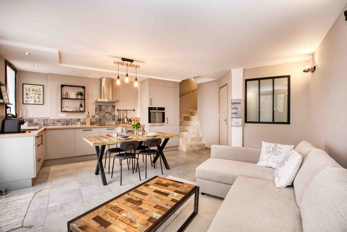 An open-plan living area is present, featuring a modern kitchen with sleek cabinetry and stainless-steel appliances. A dining table is set with chairs, and a cozy sofa is positioned beside a wooden coffee table. Soft lighting enhances the welcoming atmosphere throughout the space.