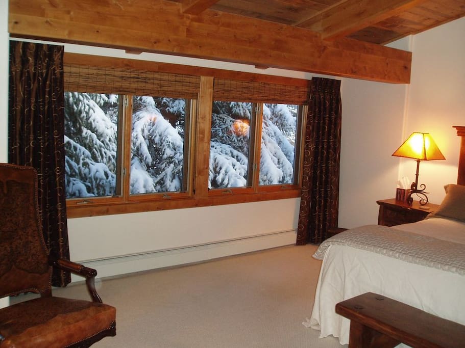 Creekside bedroom with king bed and wall of casement windows, view after a snow