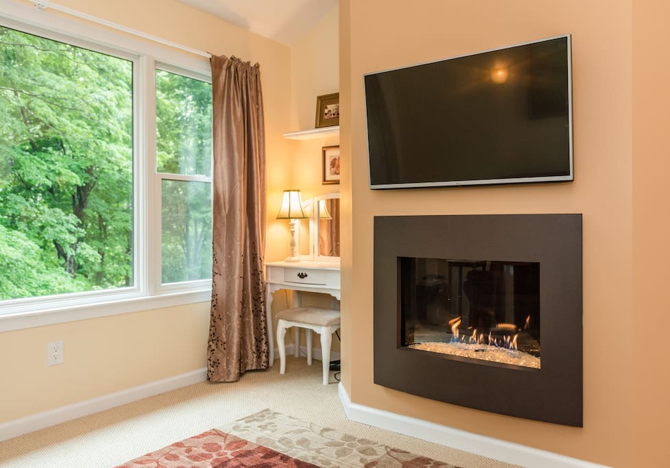 Master Bedroom sitting area with gas fireplace, flat screen TV, large picture window, and vanity