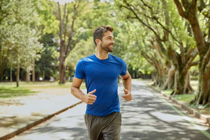 A man in a blue shirt jogs through a serene park, surrounded by lush greenery