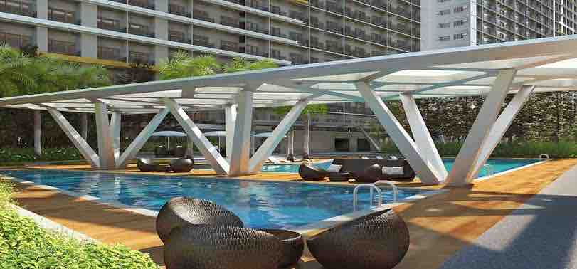 An outdoor swimming pool area is surrounded by modern lounge chairs and greenery. A shaded structure provides comfort, while the pool glistens under sunlight, inviting relaxation. The backdrop features the condominium building, contributing to the atmosphere of a serene urban oasis.