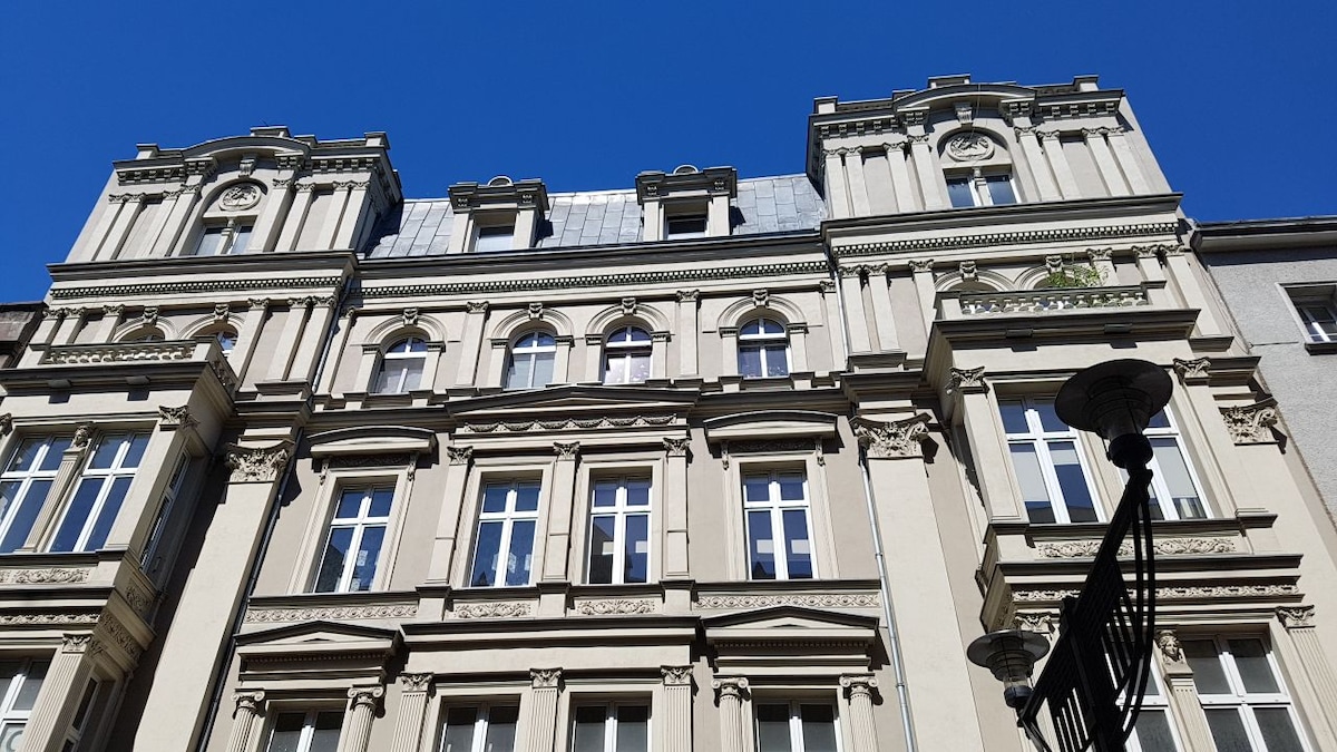 The image captures an elegant historic building, featuring intricate architectural details. Multiple windows with decorative frames are clearly visible, along with ornate elements above the windows. A bright blue sky serves as a backdrop, enhancing the building's prominent features.