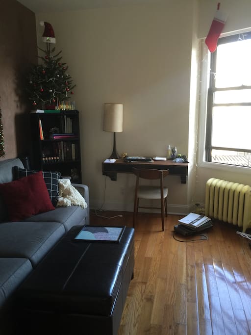 Open concept sunny living room with couch, ottoman, and desk for at-home work