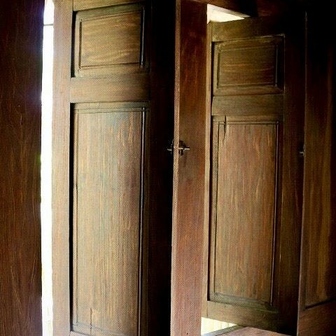 Wooden doors are depicted in the image, showcasing a rich brown finish. The doors are slightly ajar, allowing soft light to filter in, creating a warm ambiance. The detailed paneling adds a touch of classic design to the entryway.
