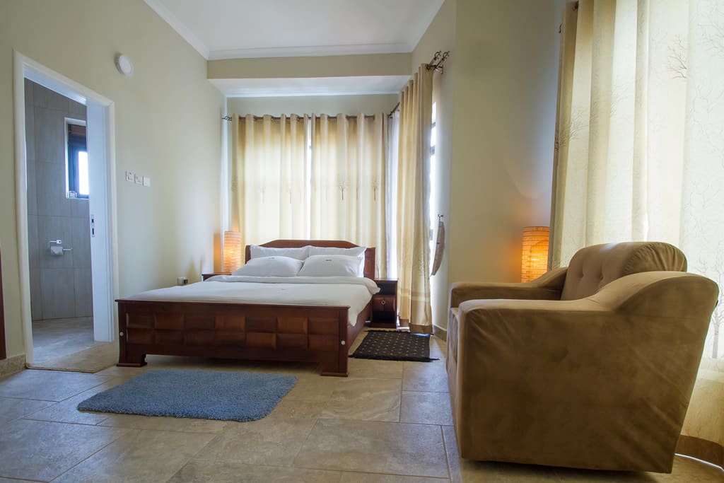 Upstairs Master Bedroom has a King-size bed, trendy bedside/desk lamps, fresh clean sheets, own modern bathroom with running hot water, and a Juliet balcony overlooking the glorious views of Kampala hills.