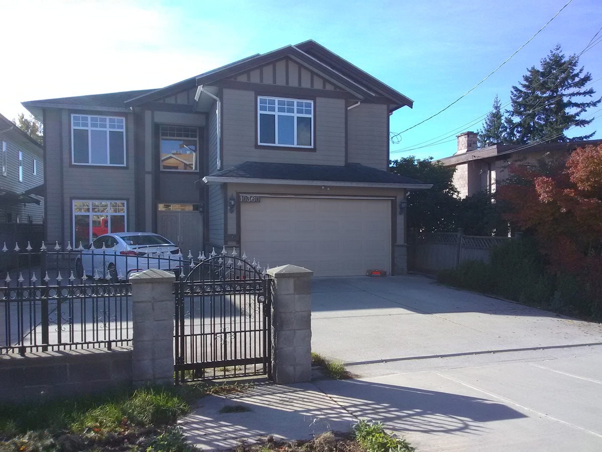 A two-story home is presented with a spacious driveway and a well-maintained front yard. The exterior features a combination of siding and stone accents. Large windows offer natural light, while a gated entrance adds to the property's privacy. Colorful foliage is visible in the foreground.