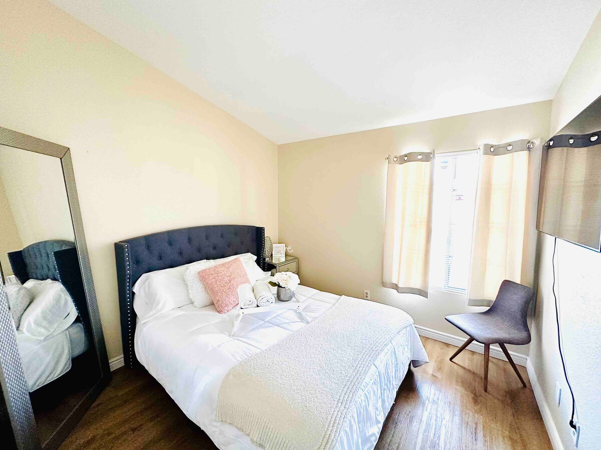 ห้องนอนแรกพร้อมเตียงควีนไซส์เตียงกลางคืนกระจกยืนและสมาร์ททีวี