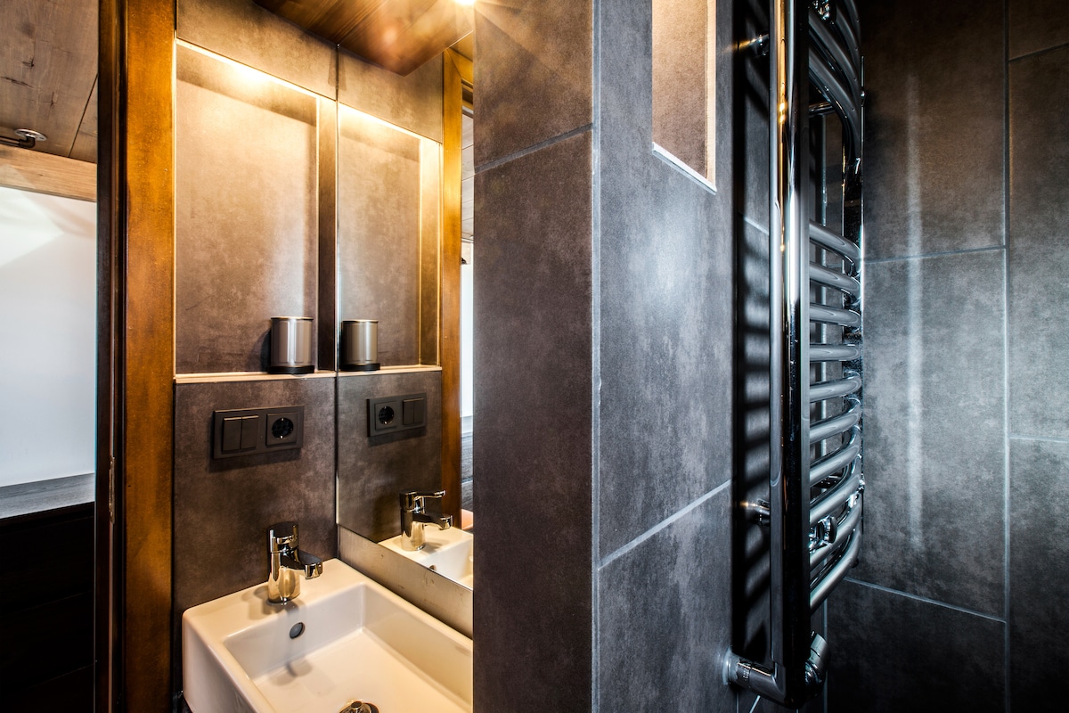 The bathroom features a modern design with sleek tile work and integrated lighting. A minimalist sink is positioned beneath a mirror, while a heated towel rail and stylish fixtures enhance functionality.