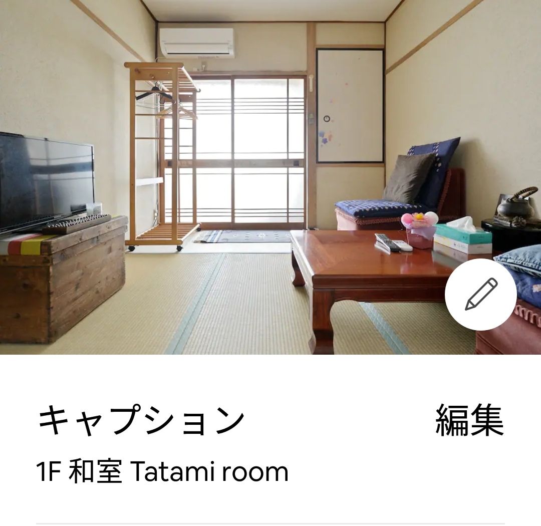 A first-floor tatami room features traditional straw mat flooring, with natural light filtering through the window. Simple wooden furnishings, including a low table and seating, complement a television and storage unit. The decor is minimal, creating a serene space for relaxation.
