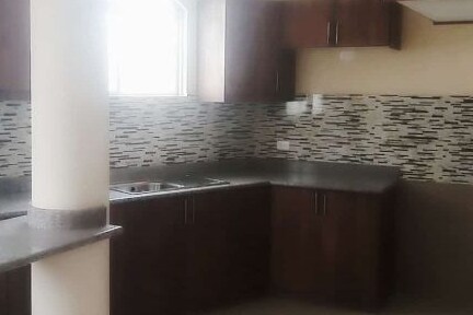 The kitchen features dark wood cabinetry complemented by a modern tile backsplash. A double bowl sink and stovetop are visible, with ample counter space for food preparation. Natural light enters through a window above the sink, enhancing the functional layout.