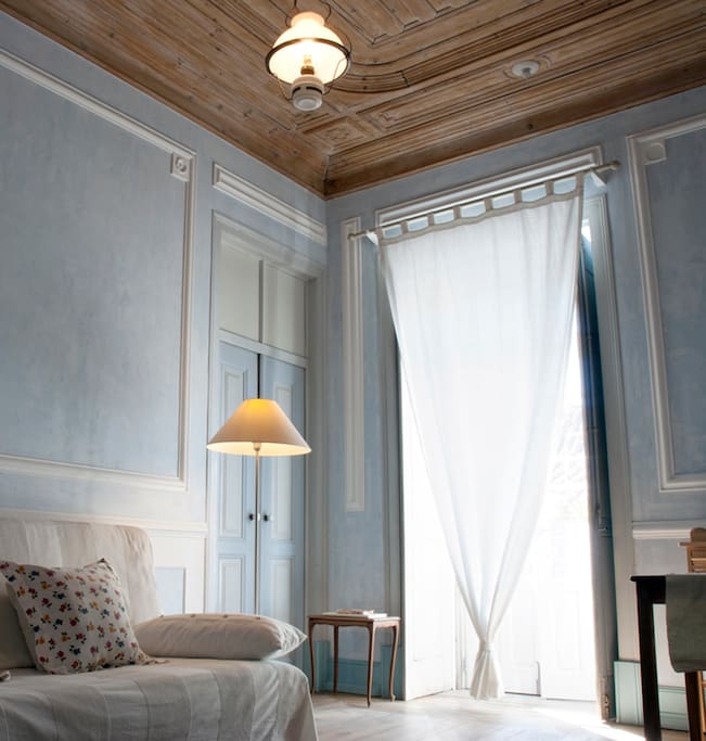 living room: french window; blue stucco render, wooden ceiling and floor.