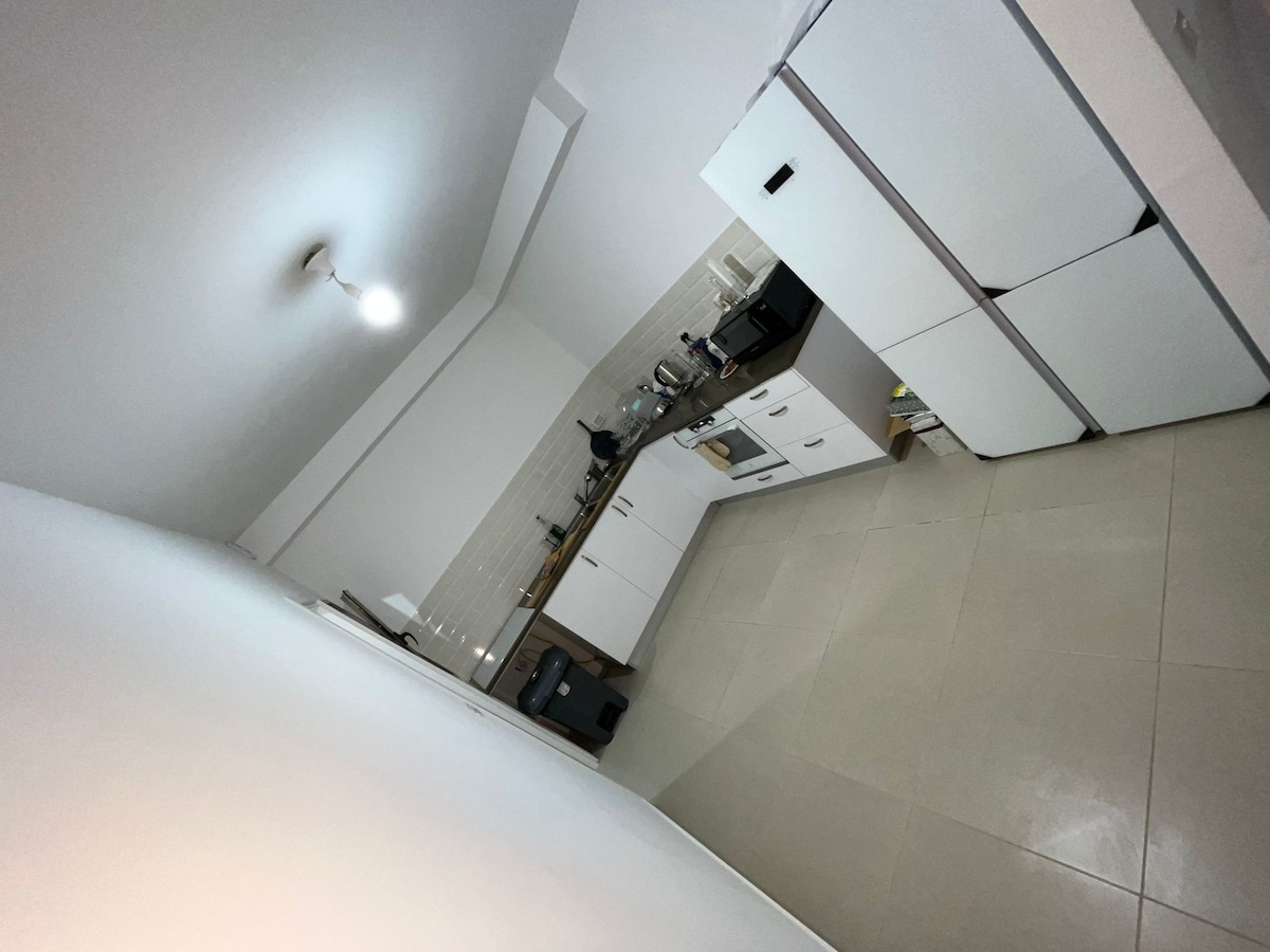 A bright kitchen space is equipped with essential appliances, including a stove and refrigerator. Countertops are neatly arranged with utensils and kitchenware. Ample cabinet storage is visible, with a modern finish enhancing the clean, functional design.