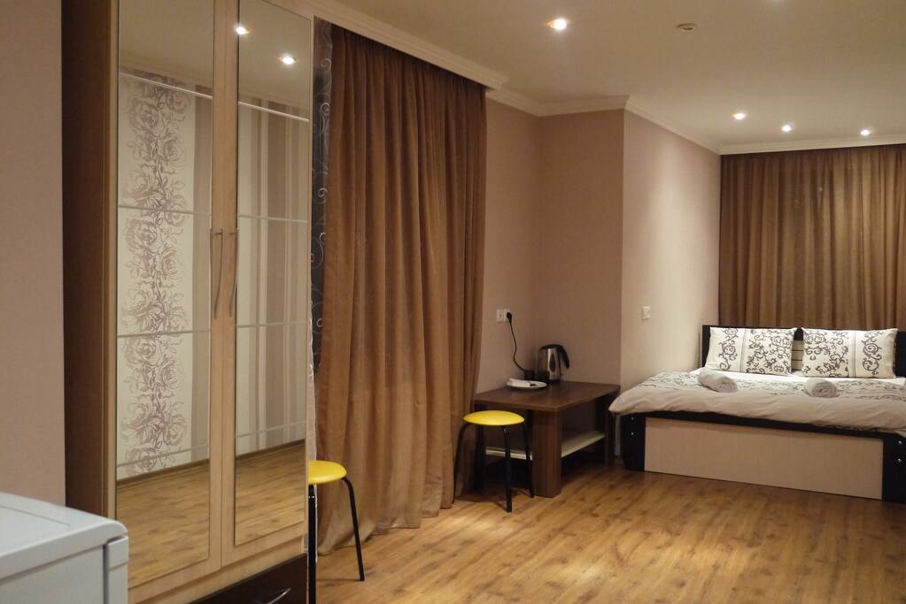 The room contains a double-bed, a wardrobe, a small fridge, a coffee table, two stools and a fan in summer.