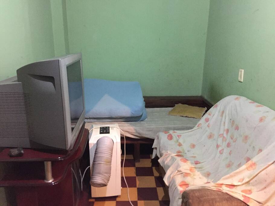 Espaço compartilhado com um sofá, e uma cama de solteiro, mais um colchão. tem ventilador na parede.