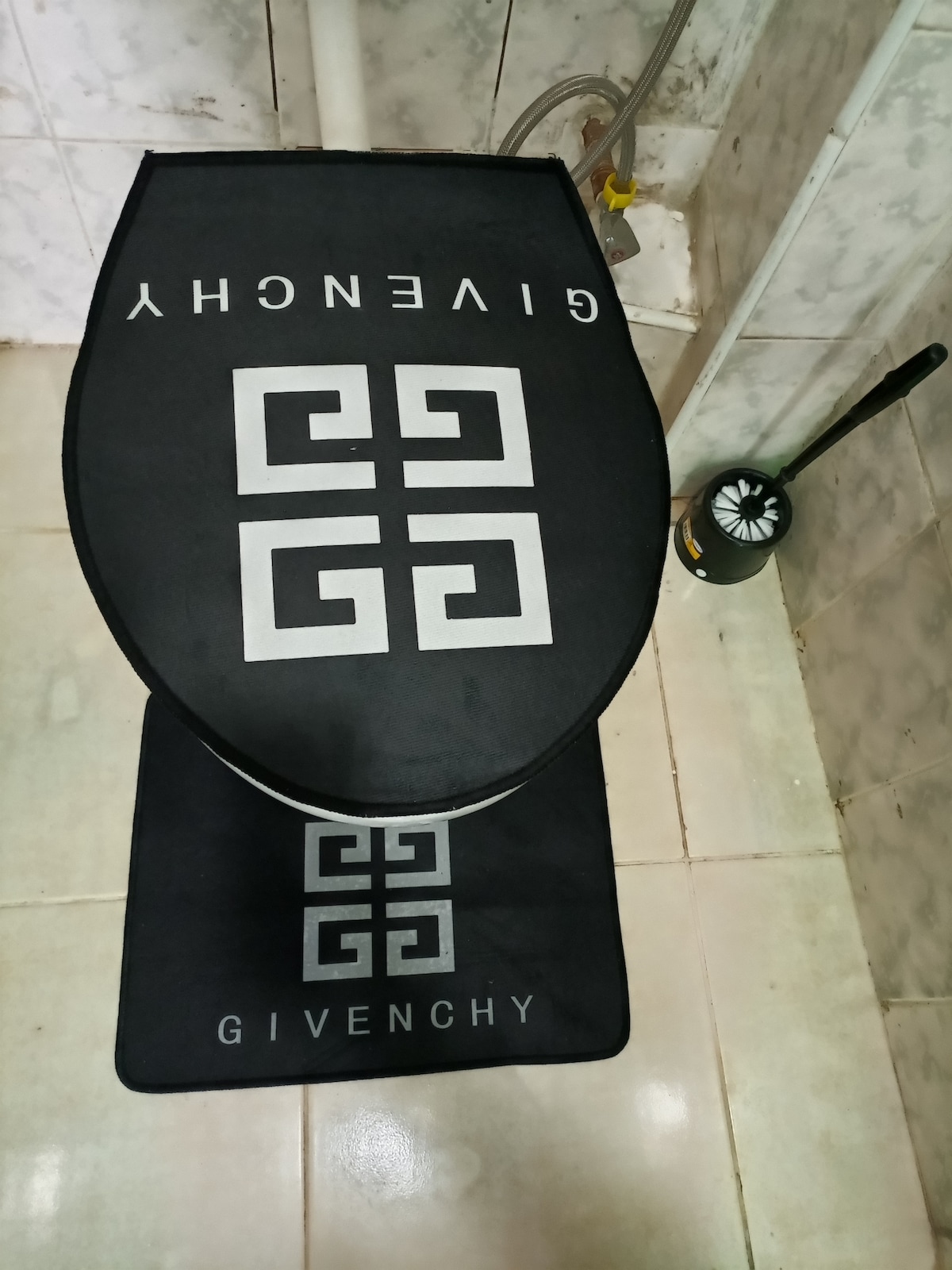The bathroom features a black toilet mat with the Givenchy logo, adding a modern touch to the space. A matching contour mat is positioned in front of the toilet. The neutral tiled floor and walls provide a clean backdrop.