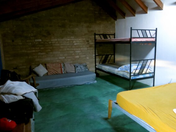 An inviting sleeping area features a spacious bed covered in a yellow blanket, alongside a gray sofa adorned with patterned cushions. A set of bunk beds is positioned against the wall, offering additional sleeping space. Exposed brick walls and wooden beams enhance the rustic charm.
