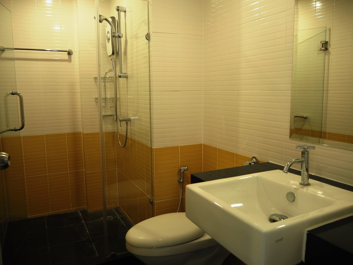 A modern bathroom is presented, featuring a glass-enclosed shower area with a handheld showerhead. A sleek white sink is installed on a dark countertop, complementing the contrasting tile colors on the walls. Ample natural light is provided through a mirror above the sink.