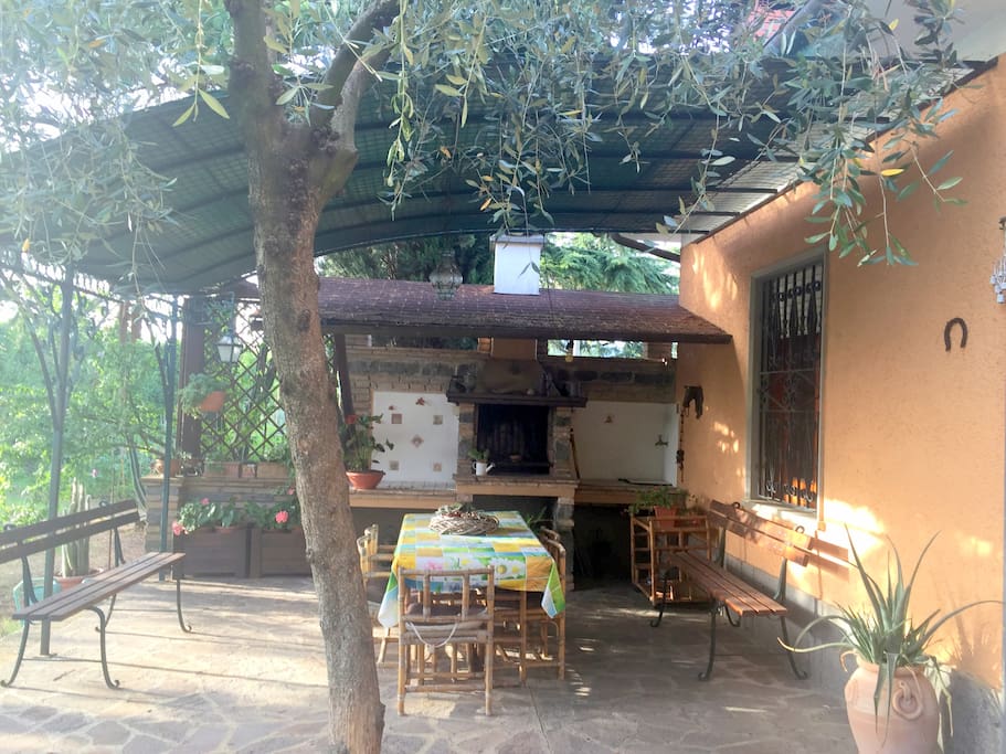 spazio esterno con veranda pavimentata e coperta, barbecue, carrello, rubinetto, tavolo e sedie fronte giardino
