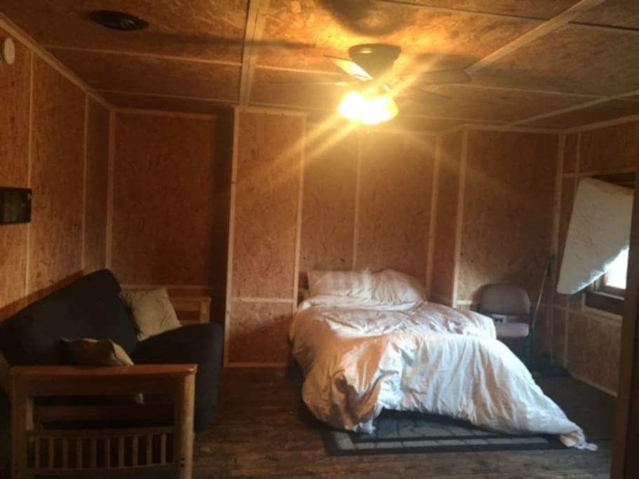 Full-size futon mattress bed, and futon sofa, ceiling fan and light shining brighly in this photo