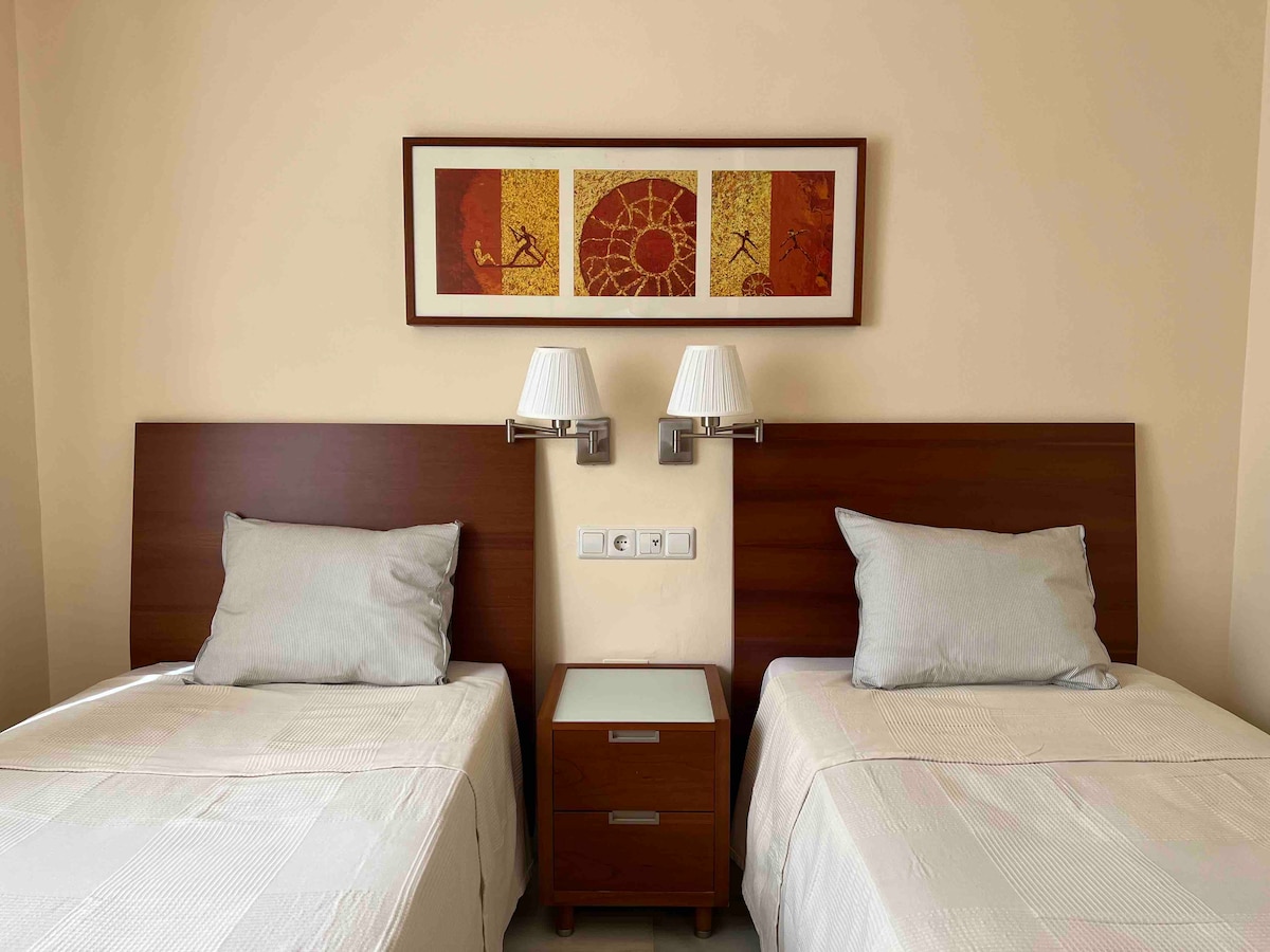 Dhoma e dytë e gjumit me dy krevate tek, ventilator tavani dhe gardërobë.
