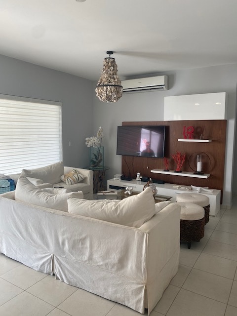 A cozy living area features a comfortable sectional sofa with beige upholstery. A flat-screen TV is mounted on the wooden wall unit, which displays decorative items. A ceiling light fixture adds a modern touch, while natural light enters through a window with subtle blinds.