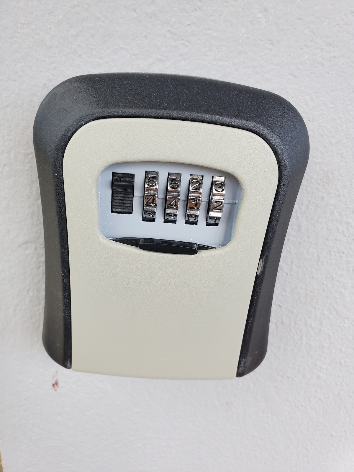 A secure combination lockbox is mounted on a wall. It features a responsive dial mechanism with five rotating number wheels, allowing for the entry of a numerical code. The design is practical, ensuring easy access while maintaining security.