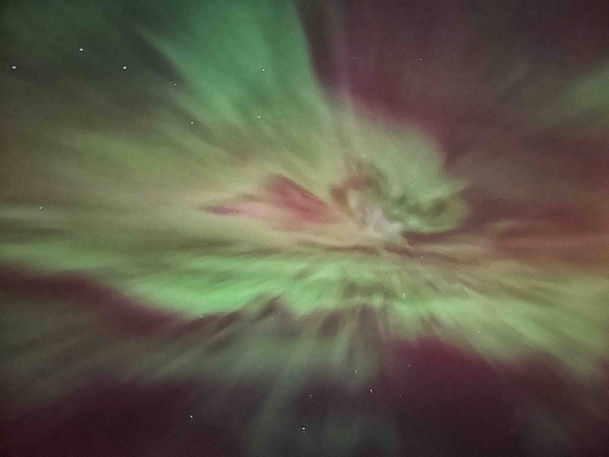 A vibrant display of the aurora borealis is captured in the night sky, featuring swirling patterns of green and hints of pink. Stars are scattered throughout the dark backdrop, creating a mesmerizing celestial scene.
