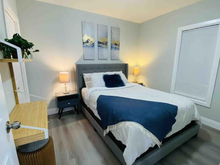 ห้องนอนแรกพร้อมเตียงควีนไซส์และโต๊ะทำงานและตู้เสื้อผ้าพร้อมลิ้นชักชั้นวางและไม้แขวนเสื้อ 