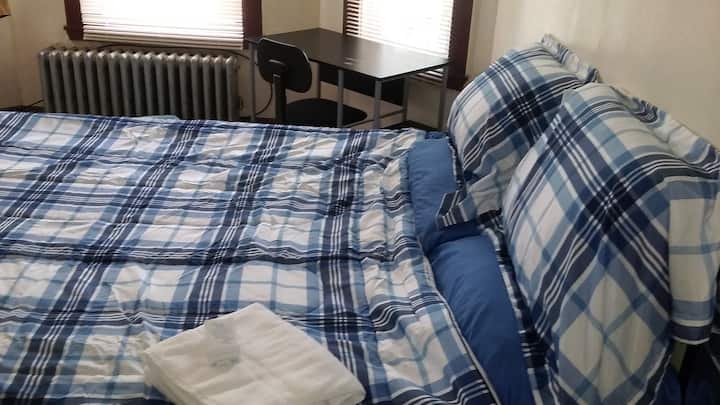 Dhoma e vizitorëve me krevat, peshqirë banje, sapun, tavolinë kompjuteri dhe karrige.