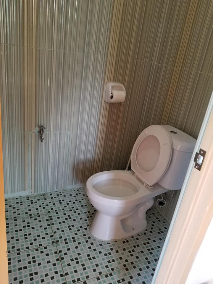 A clean bathroom is presented with a modern toilet, positioned against textured wall tiles. The floor features a mosaic pattern of small tiles, and a wall-mounted dispenser for toiletries is visible. Natural light enters through an unseen entry, contributing to a bright atmosphere.