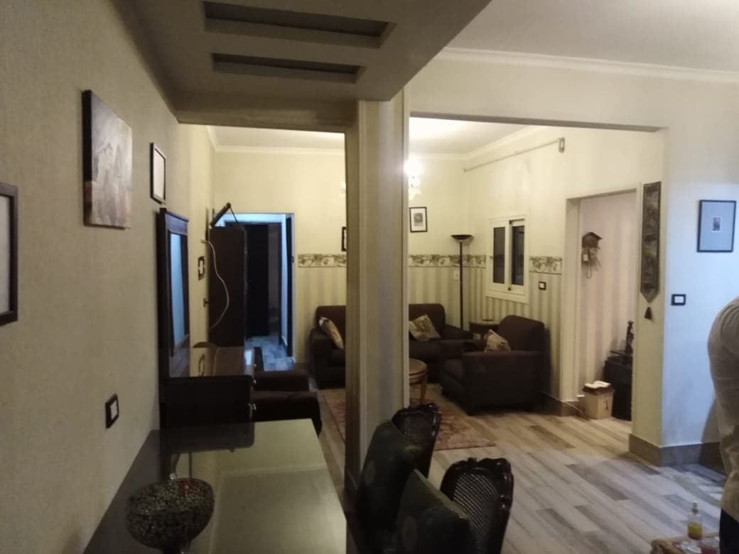 An open living area is visible, featuring comfortable seating arranged around a small area rug. A dining space with chairs is present, while light-colored walls enhance the room's brightness. Wall art and light fixtures add character to the space.