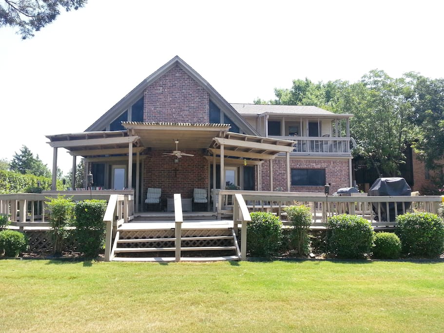 Back of house with large covered deck and multiple seating areas overlooking the lake.