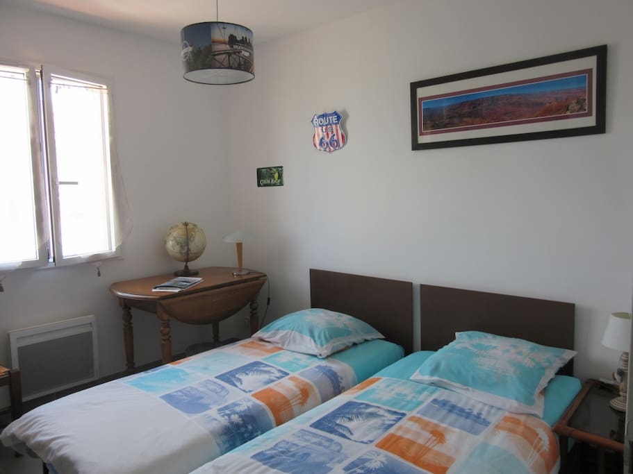 chambre claire de 2 lits d'une place avec un bureau et une armoire à glaces ( une penderie ,étagères et un tiroir )