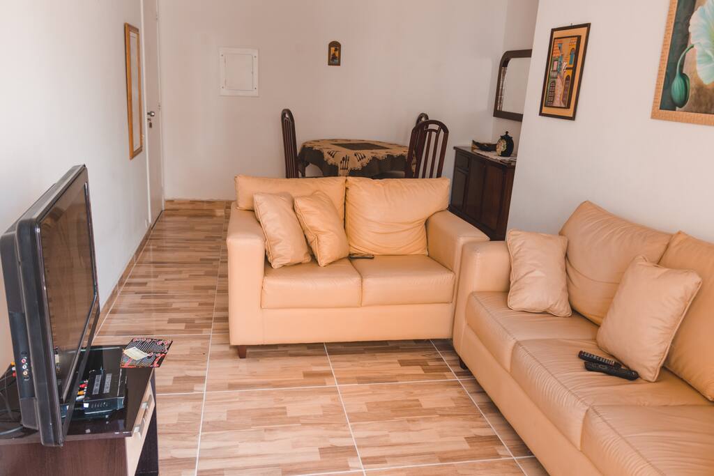 Sala ampla com sofás, tv, mesa de jantar, cortina e sacada com rede para descanso