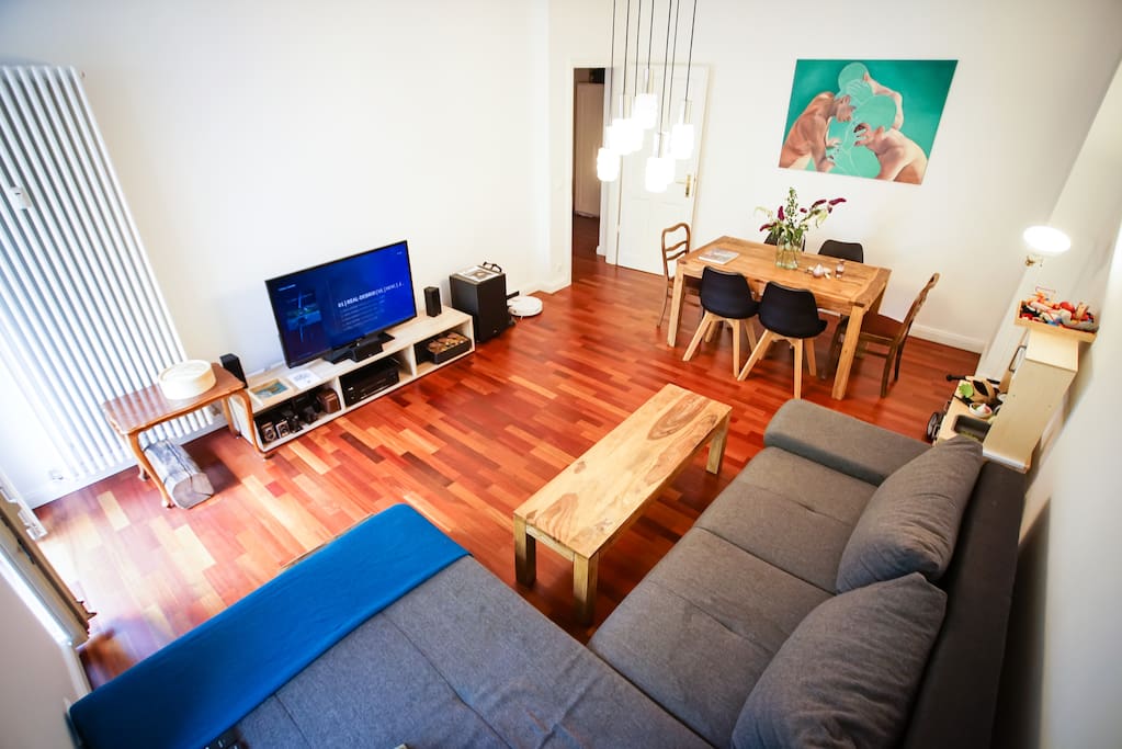 Living room with big couch, TV, dining table and access to the first balcony