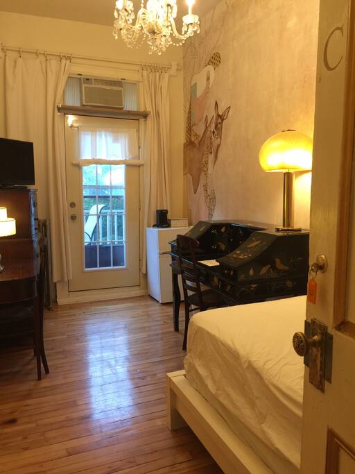 On the left are mahogany drawers with an ironing board and iron in the bottom drawer. Door leading to the deck provides beautiful daylight. There is a table and a chair on the deck. The door also has a deadbolt. Mini fridge and working/eating antique mahogany desk is also in the room.