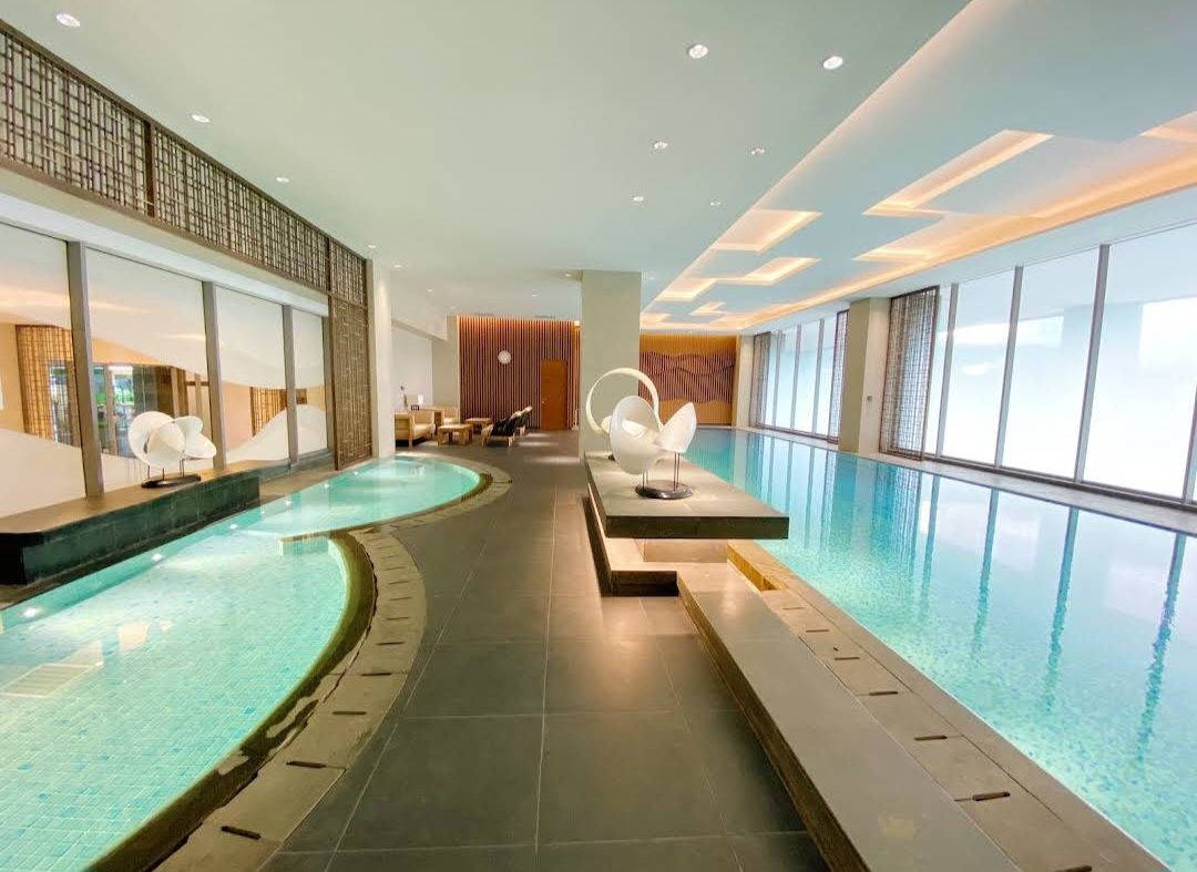 An indoor pool area is highlighted by a sleek design featuring clear water and elegant seating. Large windows allow natural light to fill the space, creating a bright and inviting atmosphere. The surrounding tile flooring is complemented by modern decorative elements.