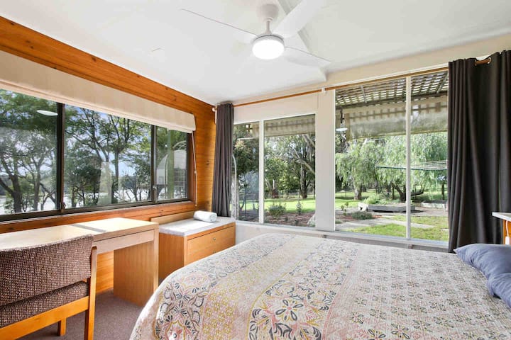 Bedroom 4 with double bed, luggage rack and desk. This room is accessed from the deck and has commanding views of the lake and gardens. On the floor plan it is labeled as the sunroom. 