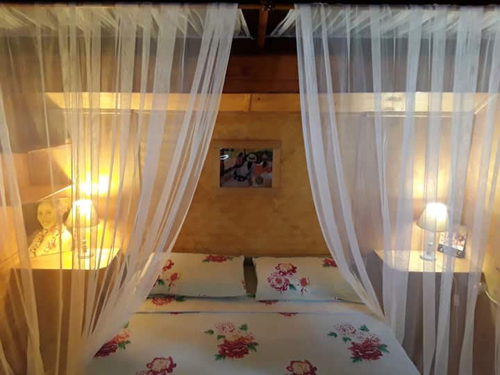 La chambre avec 1 lit de 150, ventilateur, ouvertures fenetres bois avec moustiquaires donnant sur la mer 