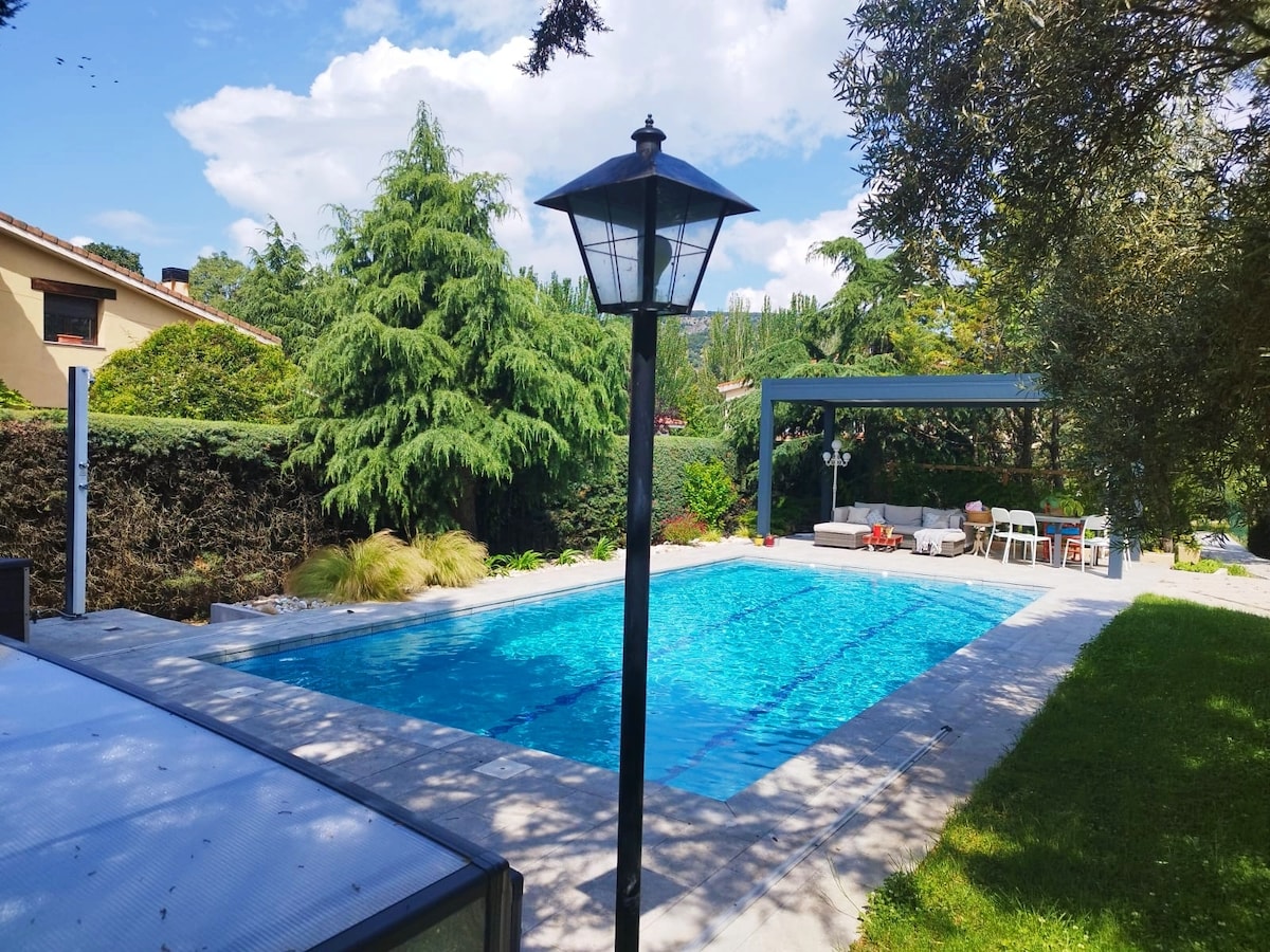 A clear swimming pool is highlighted, surrounded by a well-maintained garden featuring tall trees and lush greenery. A covered seating area with outdoor furniture is visible, alongside a patio space that accommodates multiple chairs and a table.