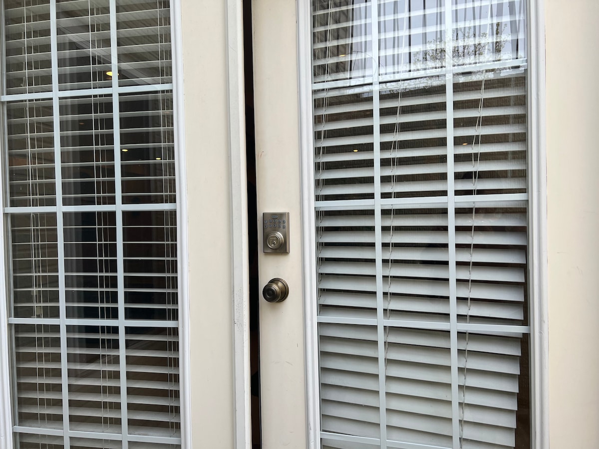 A private entrance is seen, featuring double doors with large glass panels framed by white grids. The doors are partially open, allowing a glimpse of light from the interior. A keypad for entry is positioned near the door handle.