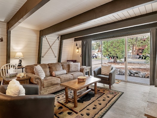 A cozy living room is illuminated by natural light from the large sliding glass door. Comfortable seating is provided with a brown sofa and armchair, paired with a rustic coffee table. A patterned area rug sits beneath, enhancing the inviting atmosphere.