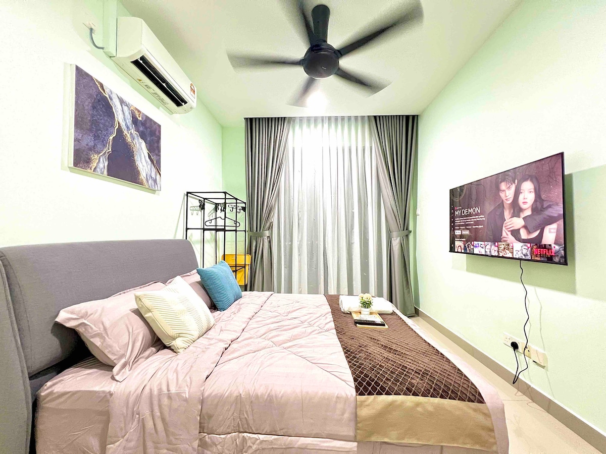 The studio suite features a spacious bed with soft linens, complemented by accent pillows. A wall-mounted TV and decorative art enhance the modern design. Natural light filters through sheer curtains, creating a relaxing ambiance. A ceiling fan adds a cooling touch to the inviting space.