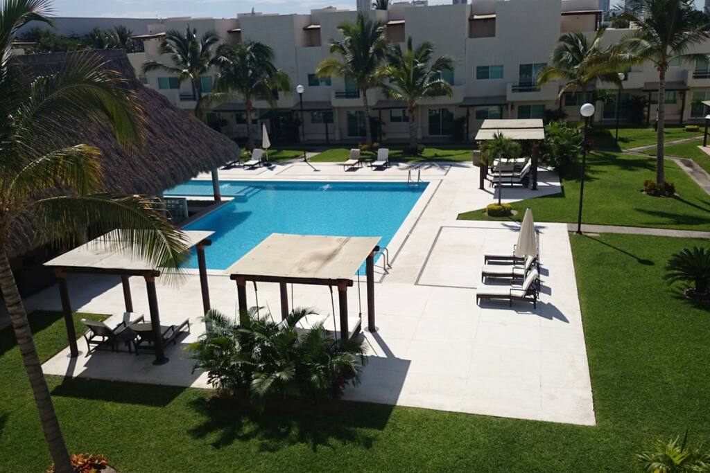 Zona de alberca, palapa, camastros y cama colgante.