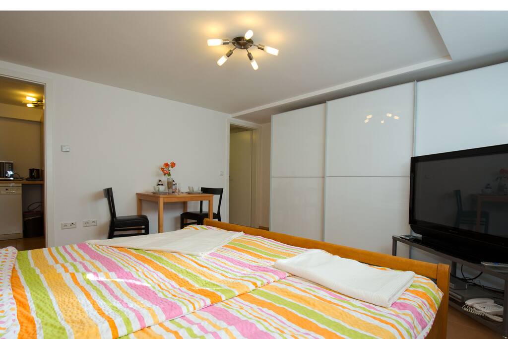 Großes Bett, großer Schrank, großer Fernseher. Links geht es zur Küche, rechts zum Bad.