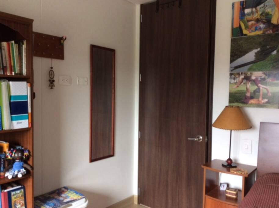 Habitación amplia con mesa de noche, espejo, lámpara y libros disponibles.
