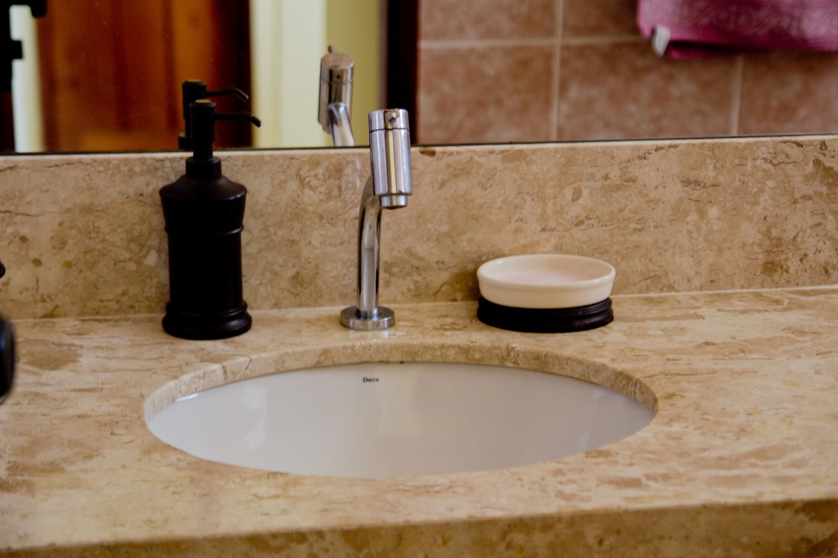 A marble countertop provides a smooth surface for a circular sink, complemented by a modern faucet. A soap dispenser and a small dish are positioned nearby, enhancing the functionality of the vanity area. The background features tiled walls in a neutral tone.