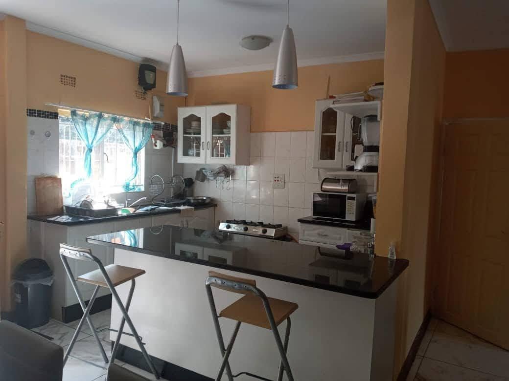 The kitchen is equipped with a spacious island counter featuring bar stools for casual dining. Cabinets provide storage space, and various appliances, including a microwave and stovetop, are visible. Natural light filters in through the window, enhancing the warm ambiance.