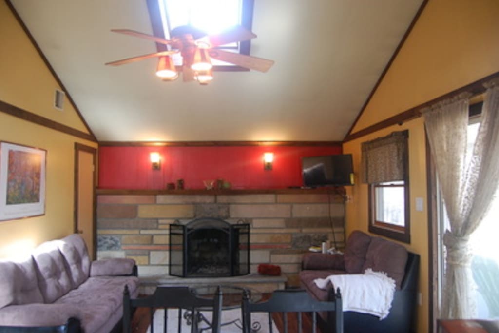 Upstairs living room with couches for 5, just off of kitchen. Features a fireplace, ceiling fan, and sliding glass door to the deck.